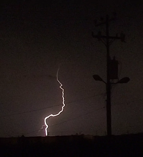 Foto de un rayo en la noche como fondo detrás de un poste eléctrico que tiene un transformador.